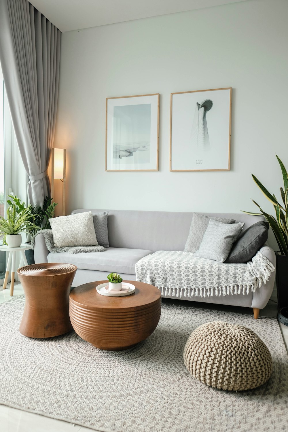A bright living room with a grey sofa, wooden side tables and fresh plants, tidy and calm